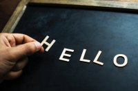 Brown hand adds and 'h' to ello already placed on a chalkboard